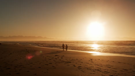 Zwei-Silhouettierte-Figuren-Laufen-Bei-Sonnenuntergang-Am-Strand-Entlang