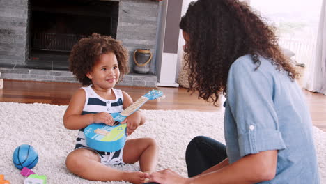 Young-black-girl-playing-ukulele-with-mum-in-sitting-room