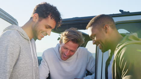 Three-young-men-on-a-road-trip-hanging-out-by-their-car
