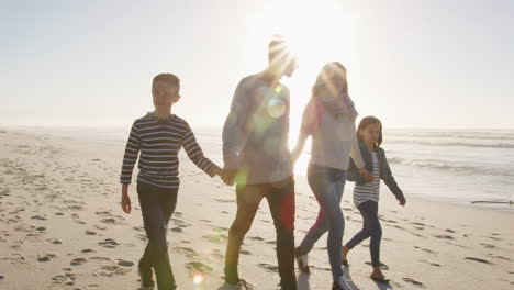 Family-Walking-On-Winter-Beach-Holding-Hands-With-Flaring-Sun