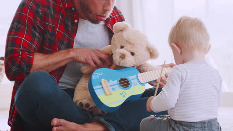 Dad-and-toddler-playing-with-instruments-and-teddy,-close-up