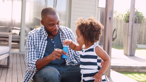 Young-black-girl-blowing-bubbles-with-dad-outside-house