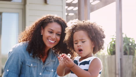 Young-mixed-race-mother-and-daughter-blowing-bubbles-outside