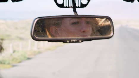 Young-woman's-face-reflected-in-mirror-of-driving-car