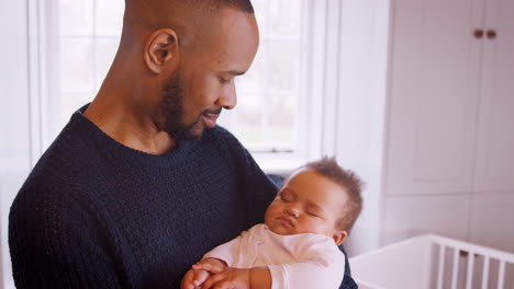 New-Father-Cuddling-Sleeping-Baby-Girl-In-Nursery-At-Home