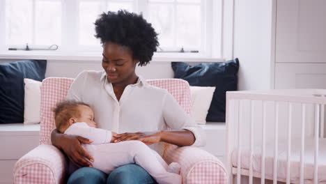 New-Mother-Sitting-In-Chair-Cuddling-Sleeping-Baby-Girl-In-Nursery-At-Home