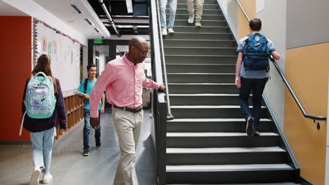 High-School-Students-And-Teacher-Walking-Down-Stairs-In-Busy-College-Building