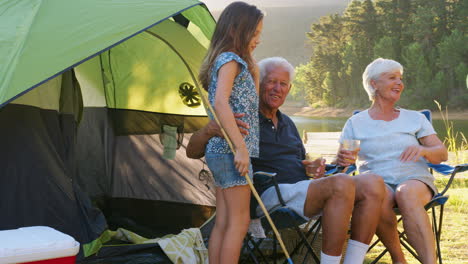 Kids-run-to-grandparents,-sitting-by-tent-in-rural-setting