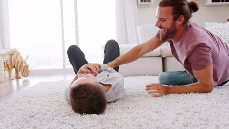 Father-Tickling-Son-As-They-Play-Game-In-Lounge-Together
