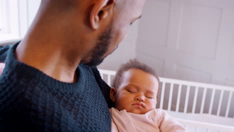 New-Father-Cuddling-Sleeping-Baby-Girl-In-Nursery-At-Home