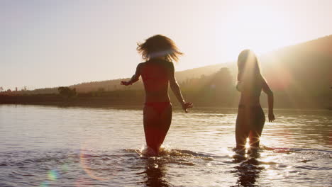 Female-friends-on-vacation-wading-out-into-a-lake-at-sundown