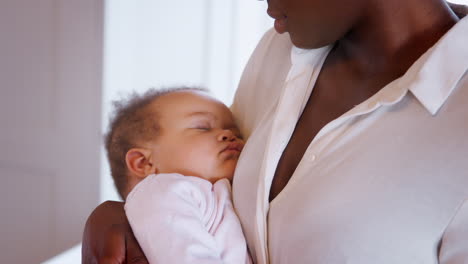 Close-Up-Of-New-Mother-Cuddling-Sleeping-Baby-Girl-In-Nursery-At-Home