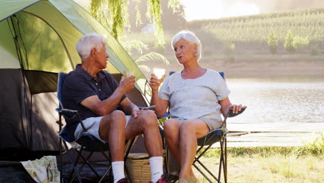 Senior-couple-on-camping-holiday-sit-by-tent-talking