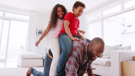Father-Giving-Children-Ride-On-Back-In-Lounge-At-Home