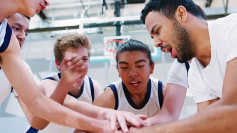 Male-High-School-Basketball-Players-Joining-Hands-On-Ball-During-Team-Talk-With-Coach