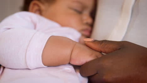 Close-Up-Of-New-Mother-Holding-Hands-With-Sleeping-Baby-Girl-In-Nursery-At-Home