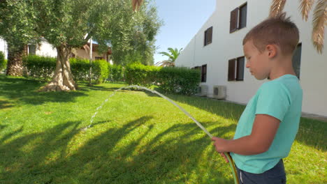 Child-taking-part-in-household-duties-and-watering-green-lawn-by-the-house