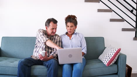 Senior-Couple-Sitting-On-Sofa-At-Home-Using-Laptop-Computer-To-Shop-Online