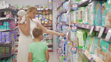 Woman-with-baby-and-elder-son-choosing-diapers-in-supermarket