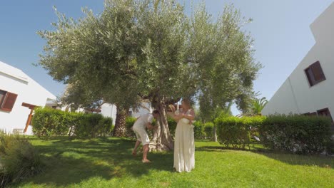 Glückliche-Eltern-Und-Kinder-Im-Grünen-Garten-Mit-Großem-Olivenbaum