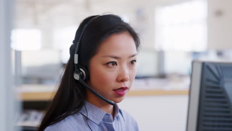 Young-Asian-woman-using-computer-in-a-call-centre,-close-up