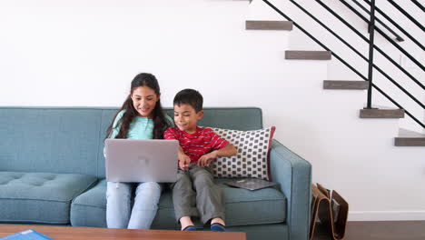Brother-And-Sister-Sitting-On-Sofa-At-Home-Using-Laptop-Computer