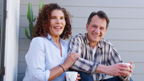 Portrait-Of-Smiling-Senior-Couple-Relaxing-Outside-Home-With-Hot-Drink