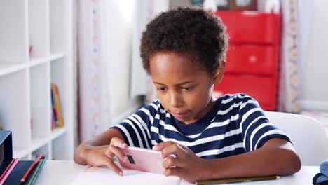 Young-Boy-Sitting-At-Desk-In-Bedroom-Playing-Game-On-Mobile-Phone