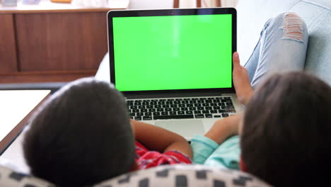Rear-View-Of-Brother-And-Sister-Lying-On-Sofa-At-Home-Using-Laptop-Computer