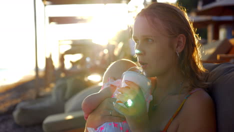 Woman-with-baby-daughter-relaxing-at-the-beach-and-having-iced-drink
