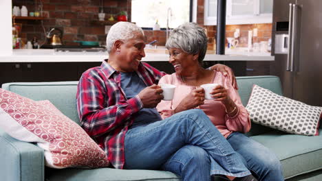 Smiling-Senior-Couple-Relaxing-With-Hot-Drink-On-Sofa-At-Home