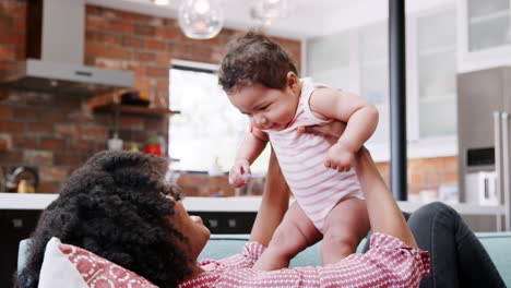 Mother-Lying-On-Sofa-And-Lifting-Baby-Daughter-Into-The-Air