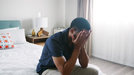 Young-Man-Suffering-With-Depression-Sitting-In-Bedroom-At-Home