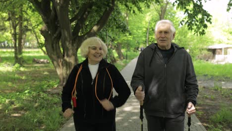 Aktives-älteres-Altes-Ehepaar.-Mann-Trainiert-Nordic-Walking,-Frau-Läuft-Im-Park