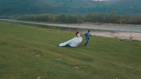 Wedding-couple-running-near-mountain-river.-Groom-and-bride.-Arial-view