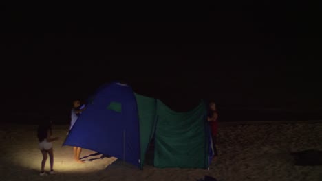 Young-people-pitching-up-the-tent-on-sea-shore-at-night