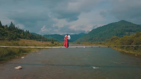 Couple-stands-on-bridge-over-a-mountain-river.-Love-of-man-and-a-woman
