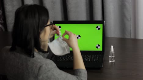 Woman-removes-medical-mask,-take-sanitizer-and-use-near-laptop-with-green-screen
