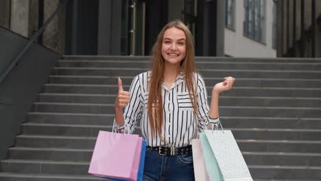 Stylish-girl-holding-shopping-bags-and-showing-thumbs-up.-Rejoicing-with-good-holiday-sale-discounts