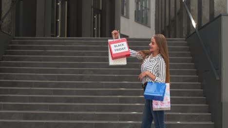 Girl-showing-Black-Friday-inscription-on-shopping-bags,-smiling,-satisfied-with-low-prices-purchases