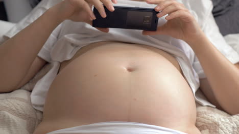 Pregnant-woman-with-bare-belly-resting-at-home-and-using-cellphone