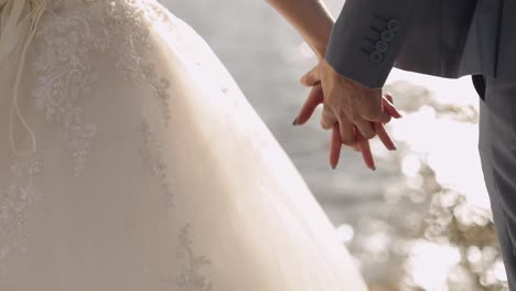Newlyweds-are-standing-by-the-sea.-They-give-each-other-hands.-Groom-and-bride