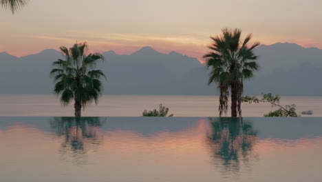 Resort-Szene-Am-Pool-Bei-Sonnenuntergang-Mit-Palmen,-Meer-Und-Bergen