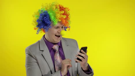 Clown-businessman-entrepreneur-in-wig-using-app-on-smartphone-for-online-work