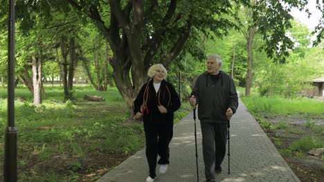 Aktives-älteres-Altes-Ehepaar.-Mann-Trainiert-Nordic-Walking,-Frau-Läuft-Im-Park
