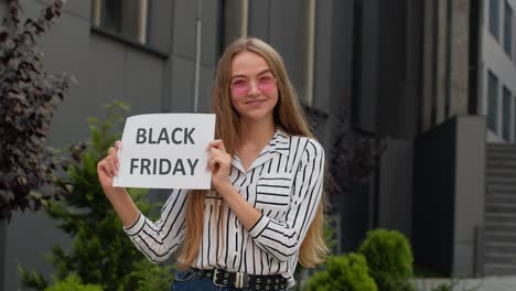 Joyful-teen-girl-showing-Black-Friday-inscription,-smiling,-looking-satisfied-with-low-prices