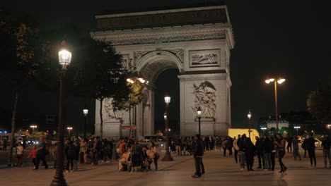 Vista-Nocturna-De-París-Con-Gente-Caminando-En-La-Plaza-Cerca-Del-Arco-Triunfal