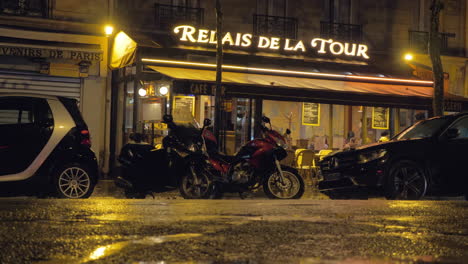 Rainy-evening-Street-with-parked-cars-motorbikes-and-roadside-cafe