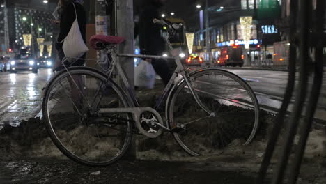 Bicicleta-En-La-Calle-De-La-Gente-De-La-Ciudad-De-Invierno-De-Noche-Y-El-Tráfico-De-Transporte-En-Segundo-Plano.