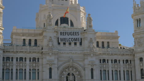 Cybele-Palace-with-Refugees-Welcome-banner-and-Plaza-de-Cibeles-in-Madrid-Spain
